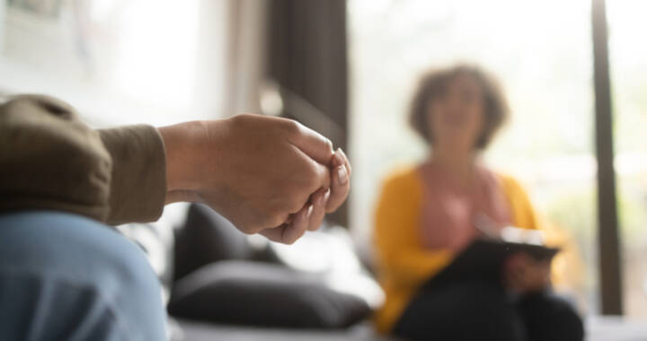 Person sitting with hands folded while counselor looks on in background